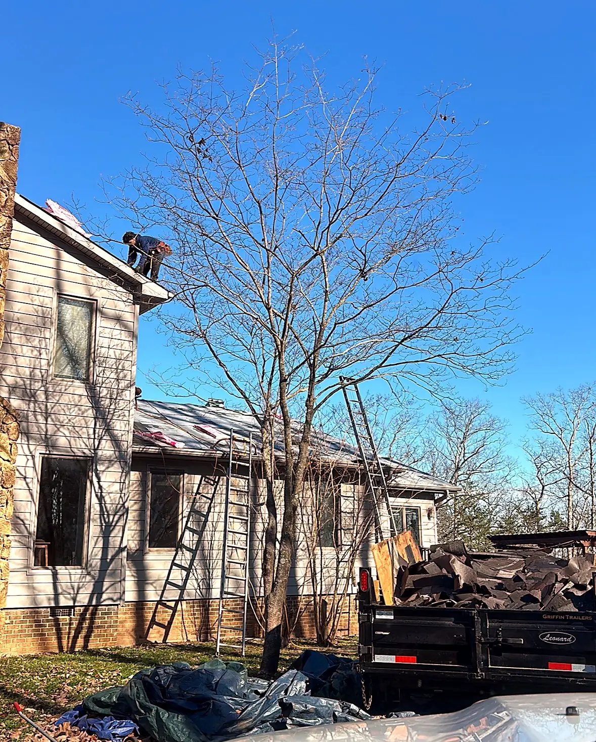 Roofer working on a roof edge while old shingles fill a dump trailer below, Kings Mountain NC